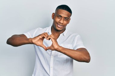 Gündelik beyaz tişört giyen genç siyah bir adam aşıkken gülümsüyor. Elleriyle kalp sembolü yapıyor. romantik kavram. 