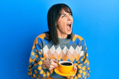 Bir fincan kahve içen Latin kökenli genç bir kadın sinirli ve kızgın çığlık atıyor ve öfkeyle bağırıyor. öfke ve agresif konsept. 