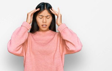 Güzel, genç Asyalı bir kadın stresten dolayı elleri başının üstünde sıradan bir kazak giyiyor. migren ağrısı. 