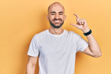 Genç, kel bir adam, günlük beyaz tişört giyiyor gülümsüyor ve el hareketleriyle el hareketi yapıyor, parmaklarıyla işaret yapıyor ve kameraya bakıyor. ölçüm kavramı. 