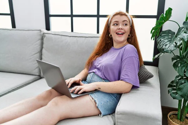 年轻的红头发女人在家里用笔记本电脑充满自信地微笑 — 图库照片