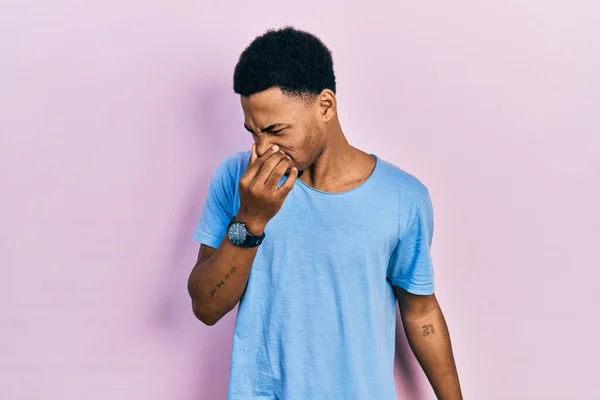 若いアフリカ系アメリカ人の男性は カジュアルなブルーのTシャツを着て鼻の上に指で息を保持し 臭いと嫌な 耐え難い匂い何かを嗅ぐ 臭いが悪い — ストック写真