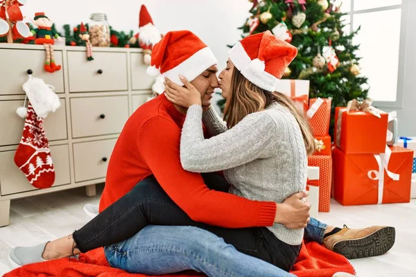 Młoda Para Świątecznym Kapeluszu Całowaniu Siedząc Podłodze Przytulając Się Domu — Zdjęcie stockowe
