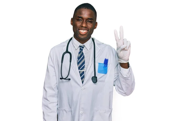 医者の制服を着た若いアフリカ系アメリカ人の男性と カメラが勝利サインをするのを見て 幸せそうな顔をして笑っている聴診器 — ストック写真