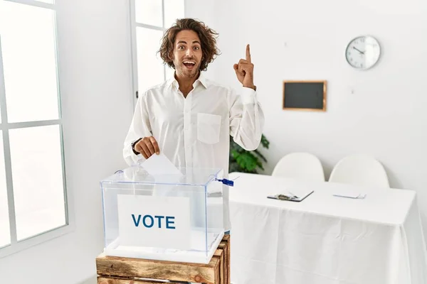 Young Hispanic Man Voting Putting Envelop Ballot Box Pointing Finger — Stock Photo, Image