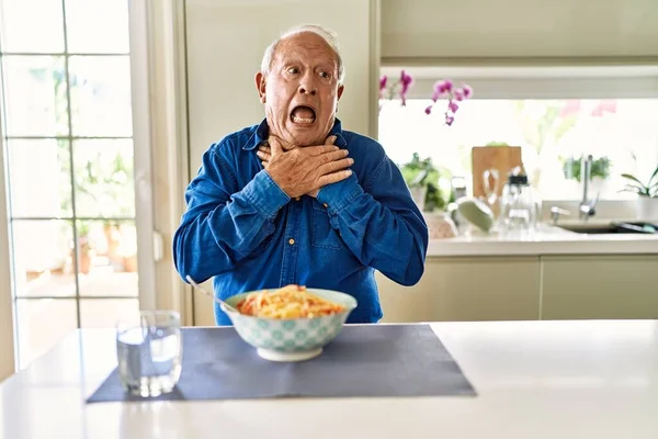 Senior man with grey hair eating pasta spaghetti at home shouting and suffocate because painful strangle. health problem. asphyxiate and suicide concept.