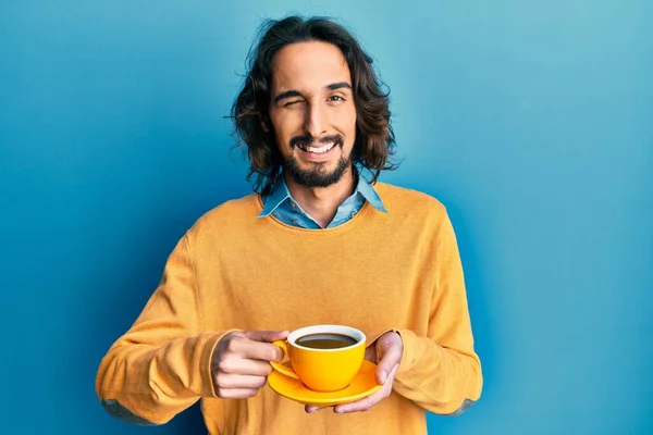 Joven Hispano Bebiendo Una Taza Café Guiñando Ojo Mirando Cámara —  Fotos de Stock