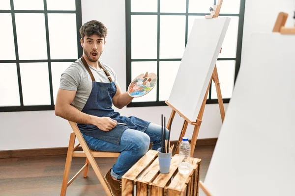 Young Hispanic Man Painting Art Studio Scared Amazed Open Mouth — Foto Stock