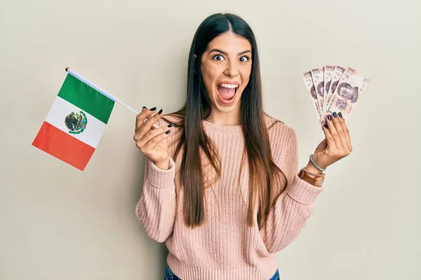 メキシコの国旗とメキシコのペソ紙幣を持っている若いヒスパニック系の女性はクレイジーを祝うと興奮叫んで開いて目で成功のために驚いて — ストック写真