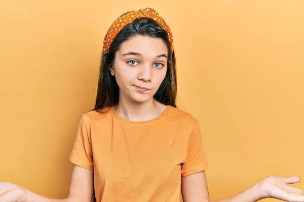 年轻的黑发女孩穿着休闲的橙色T恤 毫无头绪 满脸困惑 手臂和双手高举 怀疑概念 — 图库照片