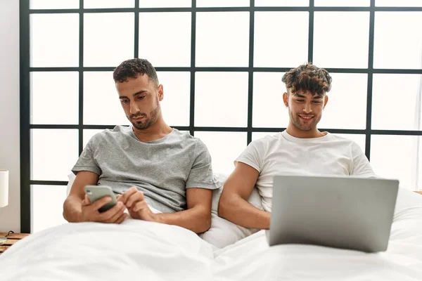 Dois Homens Hispânicos Casal Usando Laptop Smartphone Sentado Cama Quarto — Fotografia de Stock