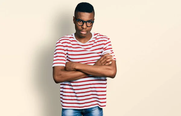 若いアフリカ系アメリカ人の男性は カジュアルなTシャツと眼鏡を着用懐疑的で緊張し 両腕を組んで顔に不承認の表現 否定的な人 — ストック写真