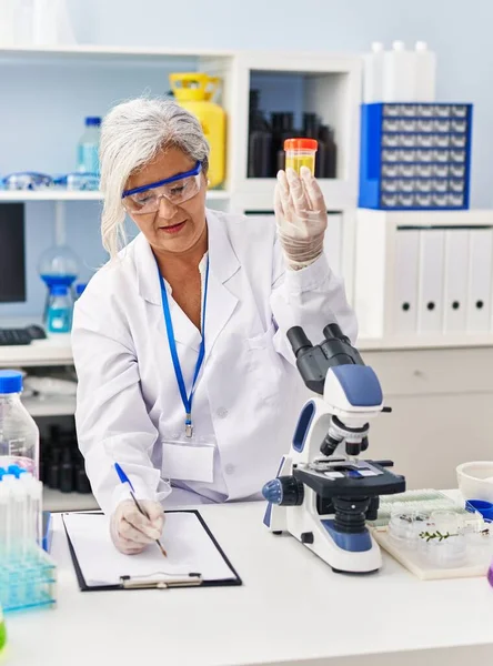 中年妇女穿着科学家制服 拿着尿检试管在实验室里 — 图库照片