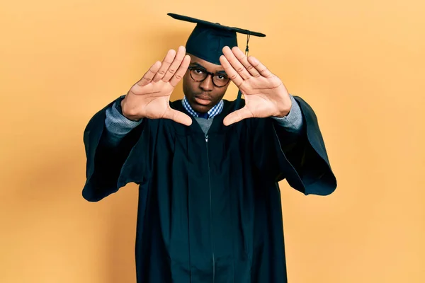 若いアフリカ系アメリカ人の男性が卒業キャップと式のローブを手の手のひらと指でフレームを行う カメラの視点 — ストック写真