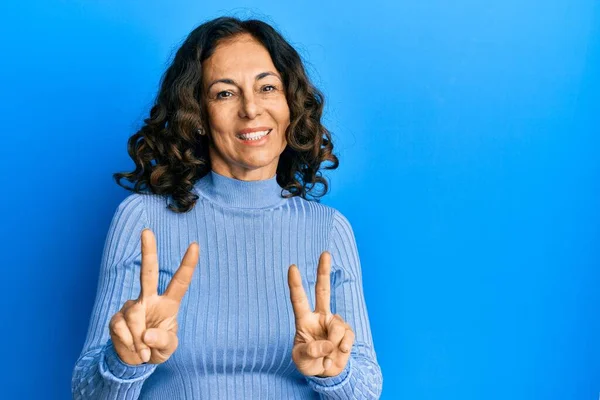 中世のヒスパニック系の女性は カジュアルな服を着てカメラに指の勝利の兆候を示す笑顔 — ストック写真