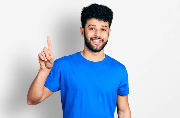 年轻的阿拉伯男子 留着胡子 穿着休闲的蓝色T恤 手指指向成功的想法 又兴奋又快乐第一大 — 图库照片