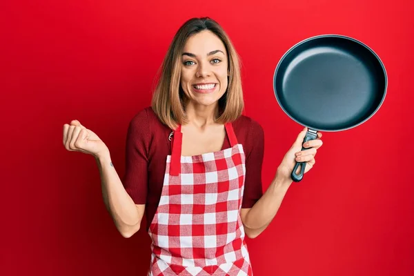 Jovem Mulher Loira Caucasiana Vestindo Avental Cozinheiro Segurando Pan Gritando — Fotografia de Stock