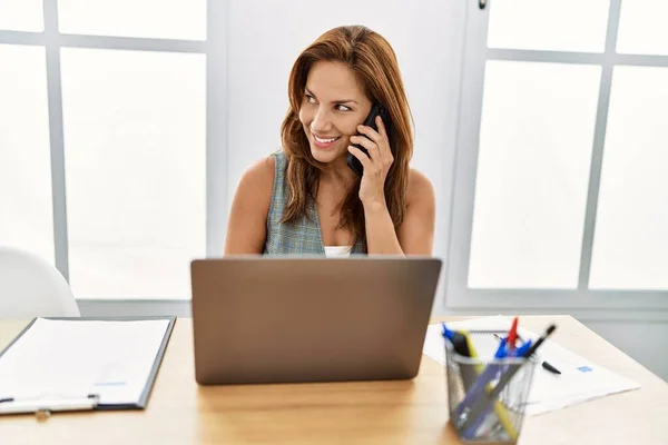 ラテン語の若い女性のビジネスワーカーがラップトップを使用してオフィスでスマートフォンで話しています — ストック写真