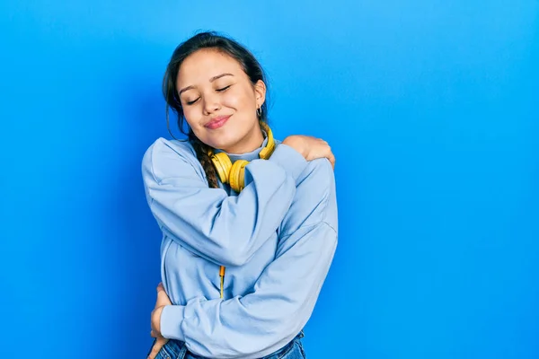 Young Hispanic Girl Listening Music Using Headphones Hugging Oneself Happy — Stock Photo, Image