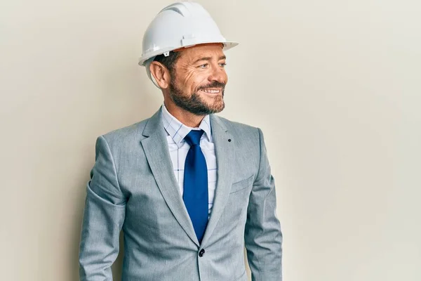 Middle age man wearing architect hardhat looking to side, relax profile pose with natural face and confident smile.