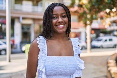 Genç Afrikalı Amerikalı kız gülümseyerek şehirde mutlu mesut duruyor..