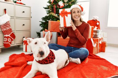 Kafkasyalı genç bir kadın elinde hediyeyle evde köpekle oturuyor.
