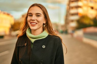 Genç sarışın kız gülümsüyor, mutlu bir şekilde şehirde duruyor..