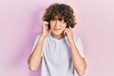 Gürültülü müzik sesi için kulaklarını parmaklarıyla kapatan günlük beyaz tişört giyen yakışıklı genç adam. sağır kavramı. 