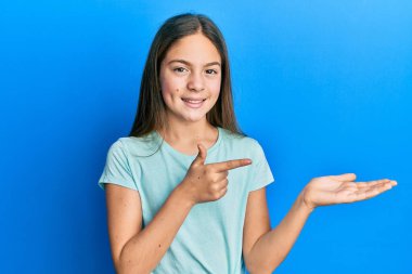 Güzel, esmer, beyaz tişört giyen küçük kız kameraya hayret ediyor ve gülümsüyor.. 