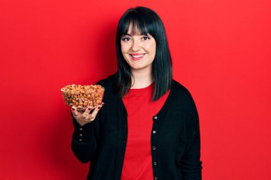 Fıstık tutan genç İspanyol kadın pozitif ve mutlu görünüyor. Durup gülümsüyor ve kendine güvenen bir gülümsemeyle dişlerini gösteriyor. 