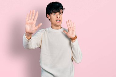 Kış süveteri giyen yakışıklı hippi genç adam korku ifadesinden korkuyor ve dehşete düşüyor. El hareketlerini bırak, şok içinde bağır. panik konsepti. 