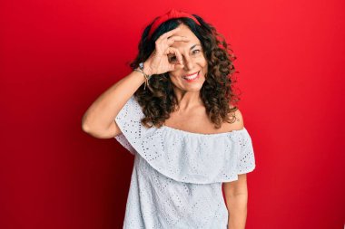 Orta yaşlı İspanyol kadın gündelik kıyafetler giyiyor. El hareketleriyle gülümsüyor, gözleriyle mutlu yüzlere bakıyor.. 