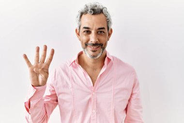 Orta yaşlı İspanyol bir adam tecrit edilmiş arka planda duruyor ve dört numarayı gösterip işaret ederken kendinden emin ve mutlu bir şekilde gülümsüyor.. 