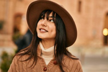 Açık havada gülümseyen, kışlık şapkalı esmer kadın.