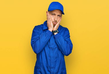 Sakallı, inşaatçı tulumu giymiş, kel bir adam. Yüzü, depresyonu ve üzüntüyü örten yorgun elleri var. Sorundan rahatsız ve sinirli. 