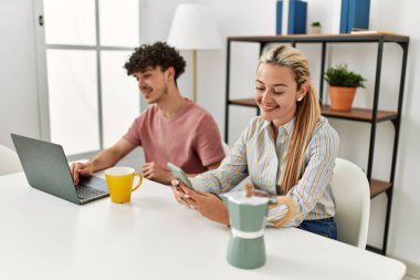 Laptop ve akıllı telefon kullanan genç bir çift evde kahve içiyor..