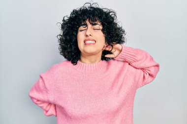 Orta Doğulu genç bir kadın günlük kıyafetler giyiyor boyun ağrısı çekiyor, boynuna elle dokunuyor, kas ağrısı çekiyor. 