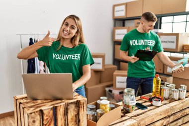 Bağışta gönüllü tişört giyen genç kadın ve erkek mutlu ve olumlu gülümsüyor, başparmağıyla mükemmel ve onay işareti yapıyor. 