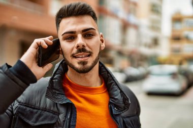 Yakışıklı, sakallı, mutlu, kendine güvenen, kışlık palto giymiş telefonda konuşan bir İspanyol.