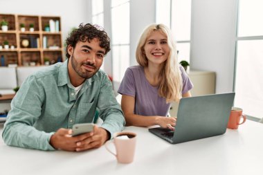 Laptop ve akıllı telefon kullanan genç bir çift evde kahve içiyor..