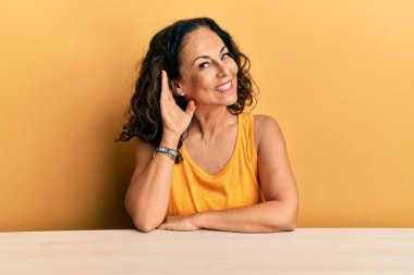 Gündelik giysiler giymiş güzel orta yaşlı bir kadın masaya oturmuş, ağzı kulaklarında oturmuş dedikoduları ve dedikoduları dinliyor. Sağırlık kavramı. 