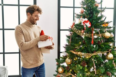 Genç İspanyol adam gülümsüyor. Evde kendine güvenen bir Noel ağacı süslüyordu.