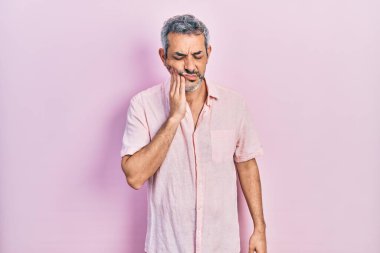 Gri tişörtlü yakışıklı orta yaşlı bir adam diş ağrısı ya da diş hastalığından dolayı elleri ve elleri ağrıyan ağızlarına dokunuyor. dişçi 