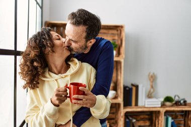 Orta yaşlı İspanyol çift öpüşüyor ve kahve içiyor. Evdeki pencereye yaslanarak.