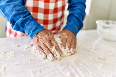 Kıdemli adam mutfakta elleriyle hamur topluyor.