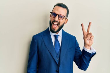 Sakallı, takım elbiseli, kravatlı, gülümseyen ve kameraya göz kırpan genç bir adam zafer işareti yapıyor. İki numara.. 