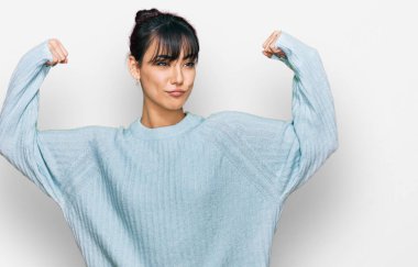 Sıradan kıyafetler giyen genç İspanyol kadın gururla gülümseyen kol kaslarını gösteriyor. fitness konsepti. 