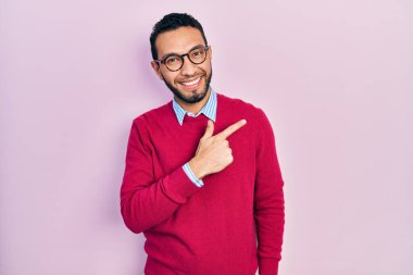 Sakallı, iş gömleği ve gözlüklü, neşeli, yüzünde gülümseme olan, mutlu ve doğal bir ifadeyle elini ve parmağını kaldırmış İspanyol bir adam. 