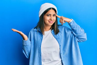 Şirin yün şapkalı genç Latin kadın avuç içi açık fotokopi alanı ve parmak alnını göstermekten rahatsız oluyor. Bunu bir düşün.. 