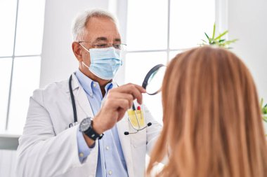 Klinikte Louise 'i kullanarak orta yaşlı erkek ve kadın doktor ve hasta tıbbi maske takıyor.